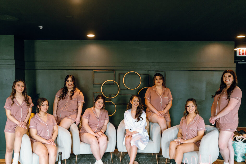 bridesmaids and bride posing for the camera, some sitting, some standing with their silk blush robes