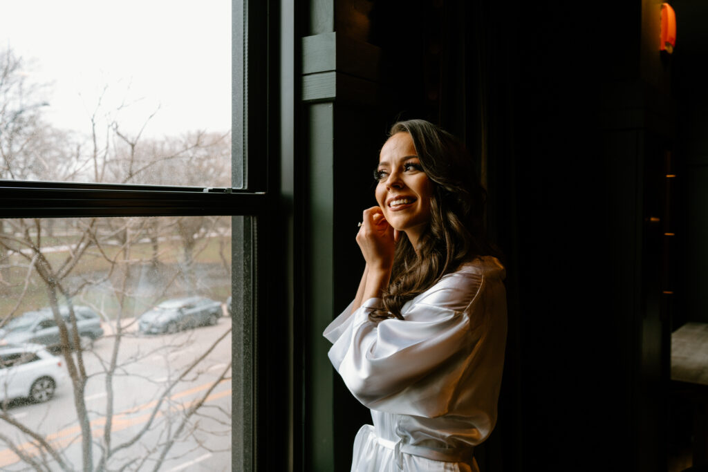 a woman looking out the window while puttin on earrings