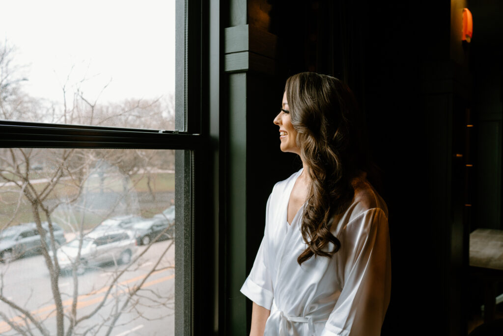 a woman looking out the window while puttin on earrings