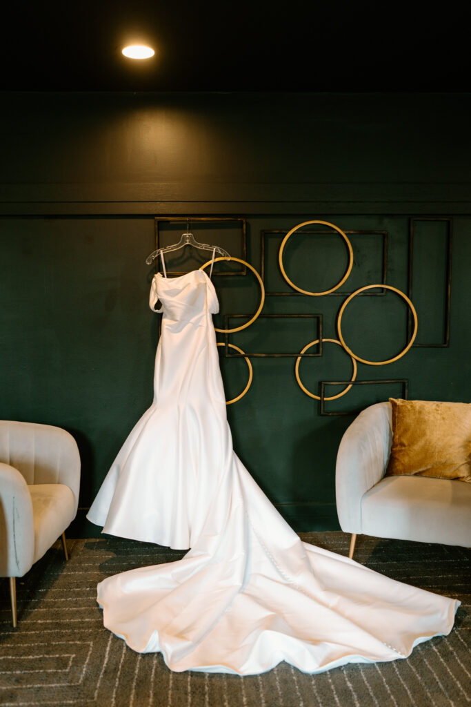 a white wedding dress with a long train hung on a dark teal wall