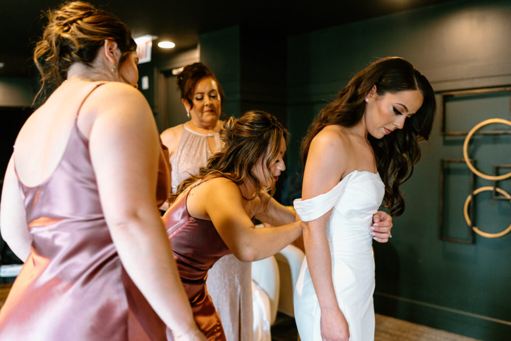 three bridesmaids helping a bride get into her dress