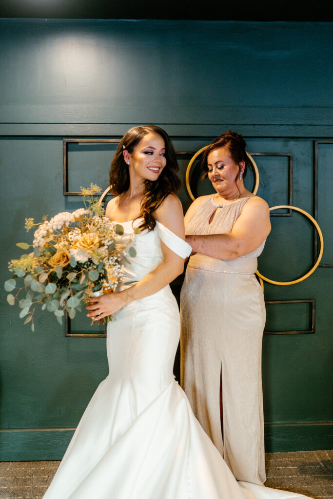 mother zipping her daughter's wedding dress as her daughter is looking back