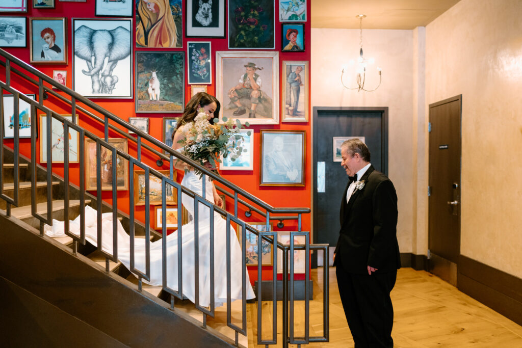 bride coming down the stairs to meet her father who is in awe