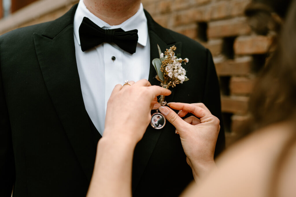 bride pinning her locket pin gift to her groom's lapel; locket containing a photo of him and his late dad