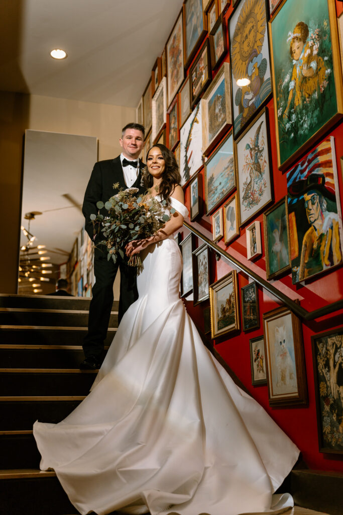 bride and groom standing in the middle of a stairway with a beautiful backdrop of a gallery wall with a red painted wall