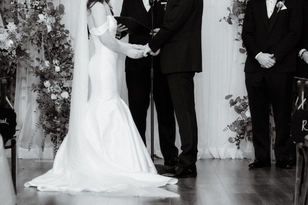 black and white photo of bride and groom holding hands in front of the altar but their heads are not inframe