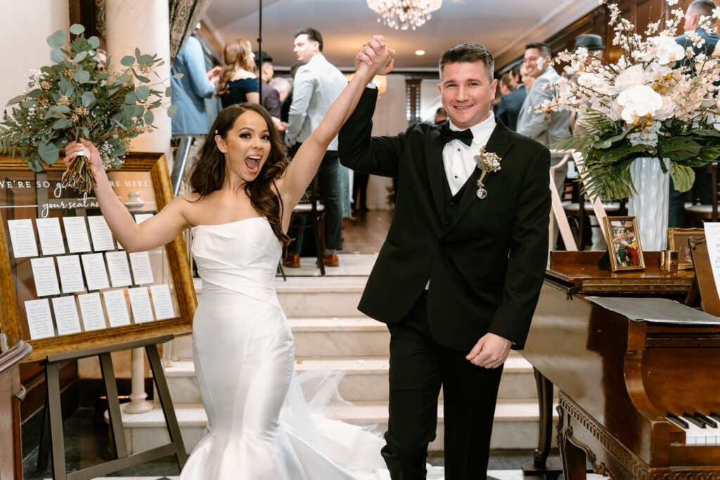 newlyweds walking towards the camera, holding hands and cheering for the camera