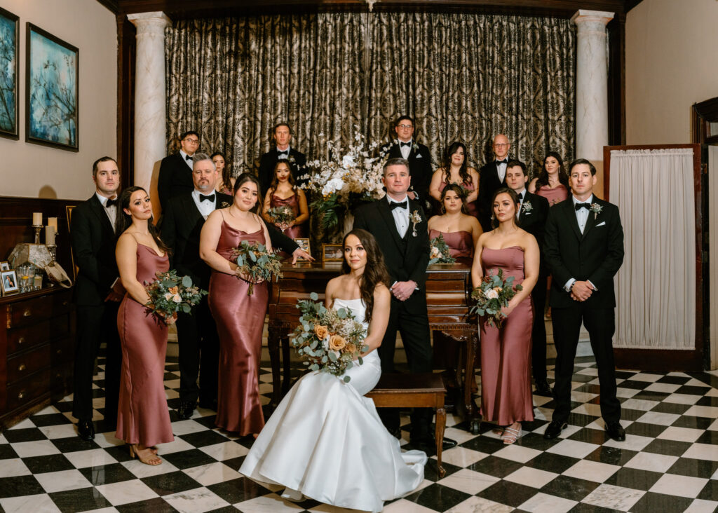 whole wedding party with the newlyweds on black and white checkered floor tiles